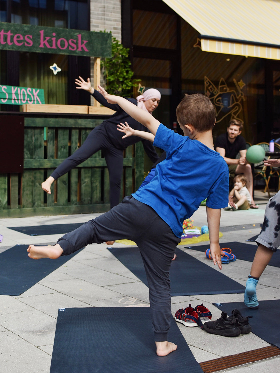 Børn og voksen laver yoga på måtter udenfor Bette Café.