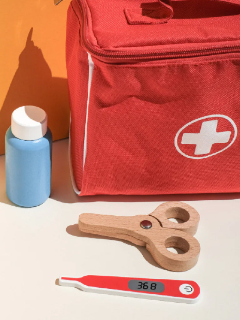 Trælegetøj med førstehjælpstaske, termometer, flaske og saks på et bord.